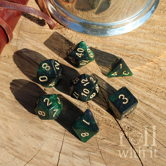 Set of 7 emerald green galaxy glitter polyhedral dice set on a wooden surface with a metallic cup in the background.