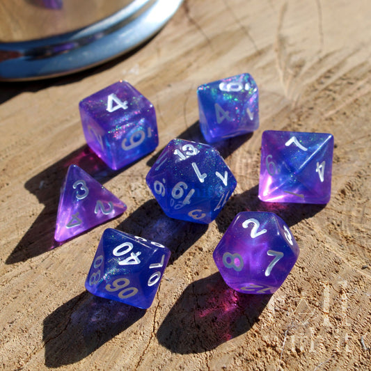 Side view of set of 7 purple and blue polyhedral TTRPG board game dice on a wooden surface