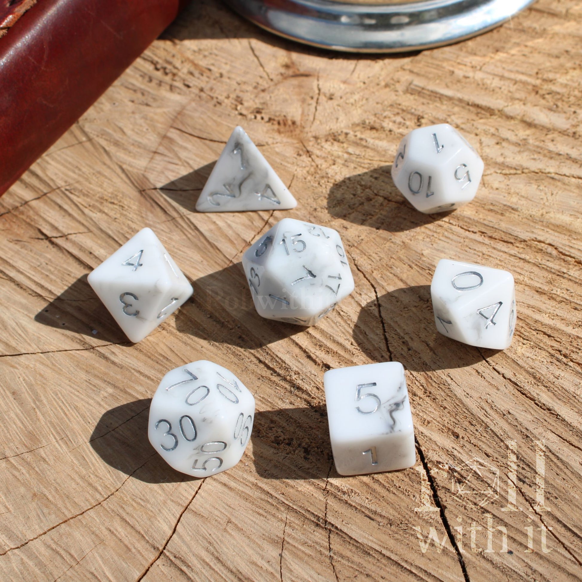 A set of 7 cool white marbled resin D&D dice on a wooden surface with silver inked numbers
