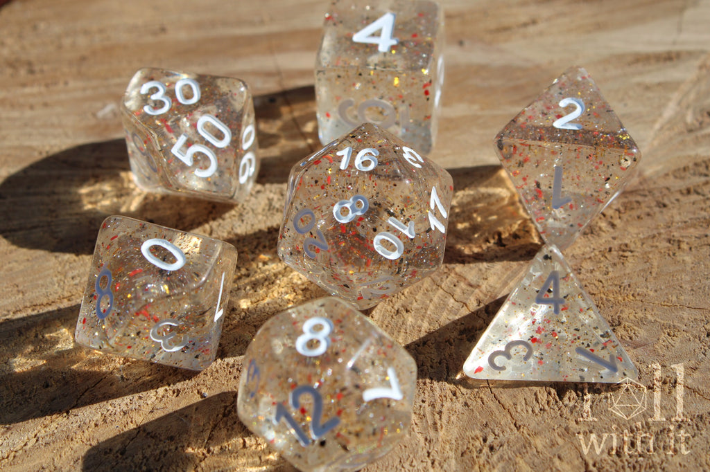 Set of clear polyhedral roleplaying dice with orange and black speckles on a wooden surface
