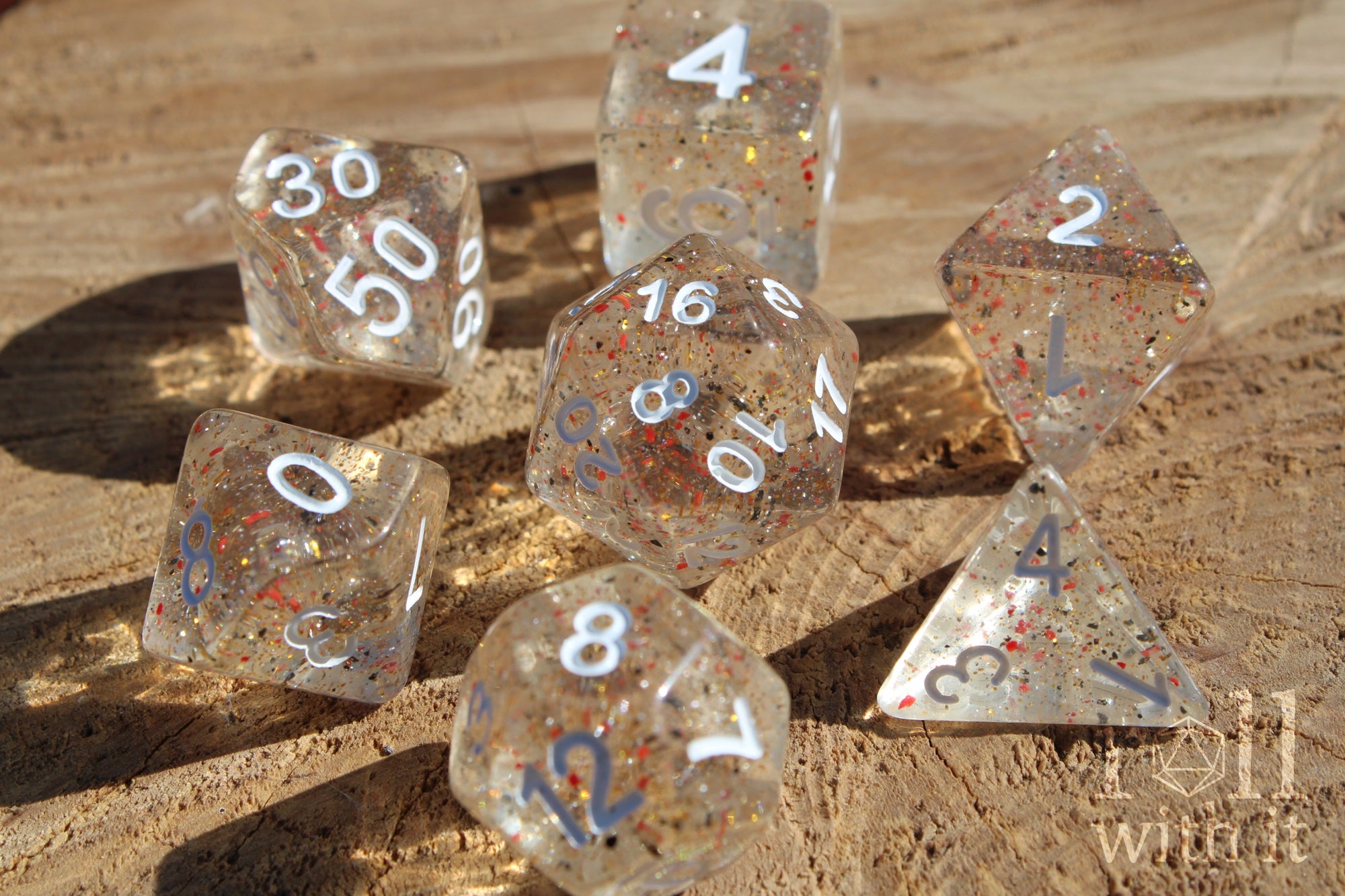 Set of clear polyhedral roleplaying dice with orange and black speckles on a wooden surface