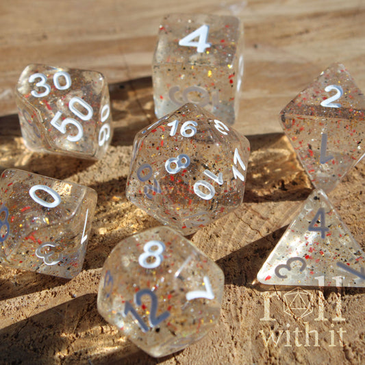 Set of clear polyhedral roleplaying dice with orange and black speckles on a wooden surface