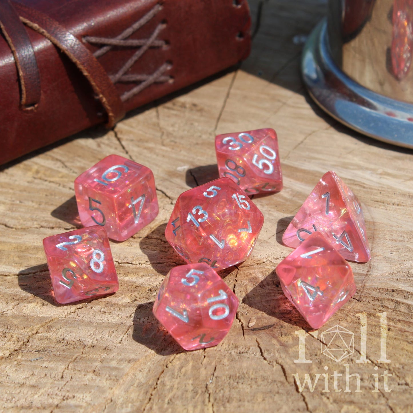 Pink reflective bright girly polyhedral dice set on a wooden surface with 'roll with it' branding.