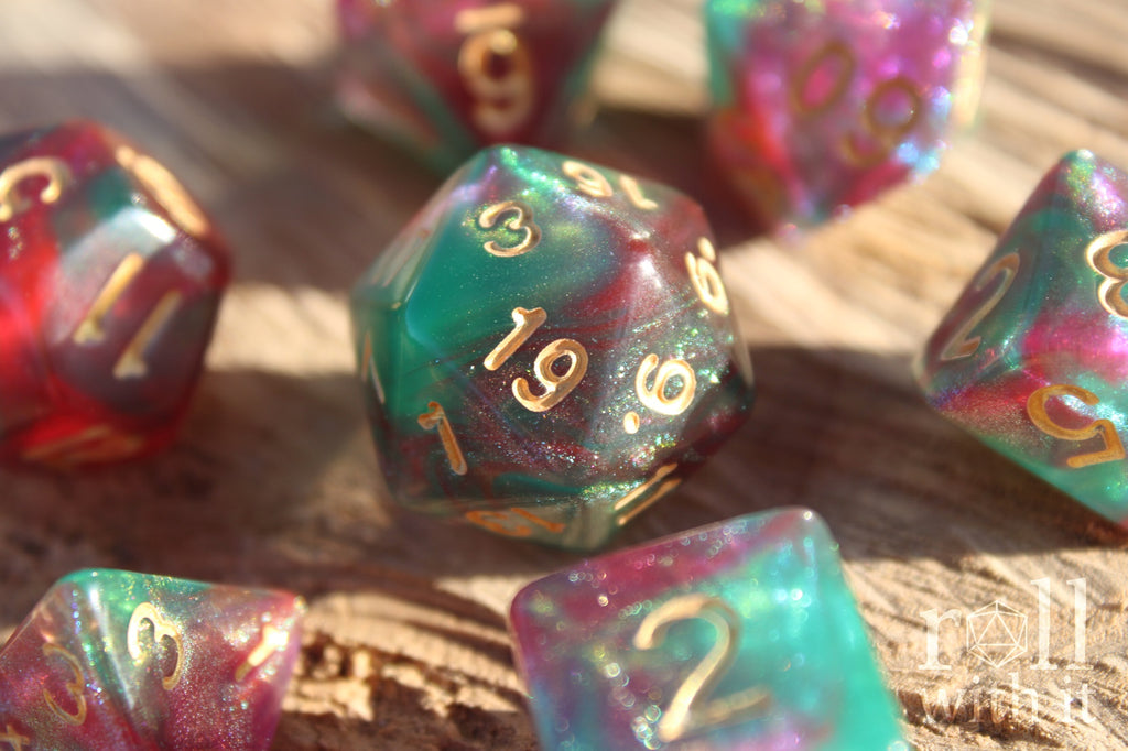 A set of 7 Faerie King polyhedral role playing dice with pink and green shimmers on a wooden table
