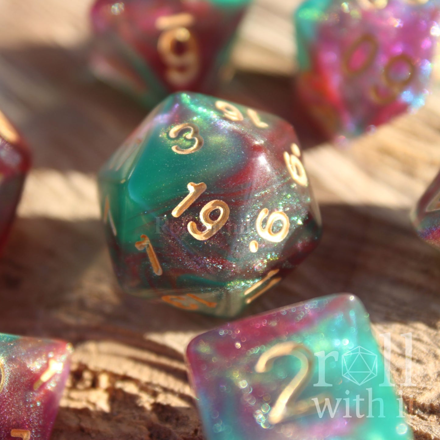 A set of 7 Faerie King polyhedral role playing dice with pink and green shimmers on a wooden table