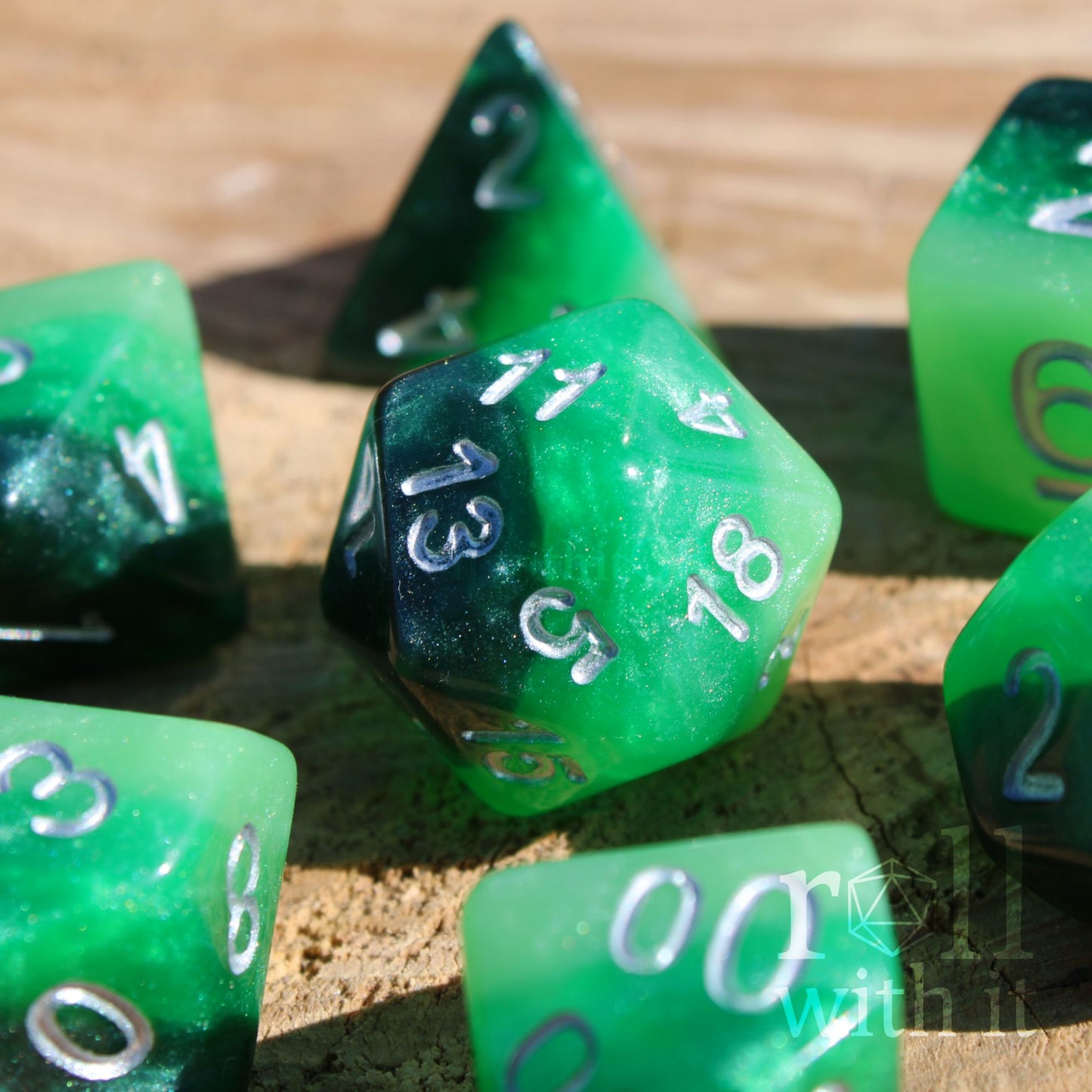 Close up of 7 green and black glittery layered polyhedral roleplaying dice set on a wooden surface