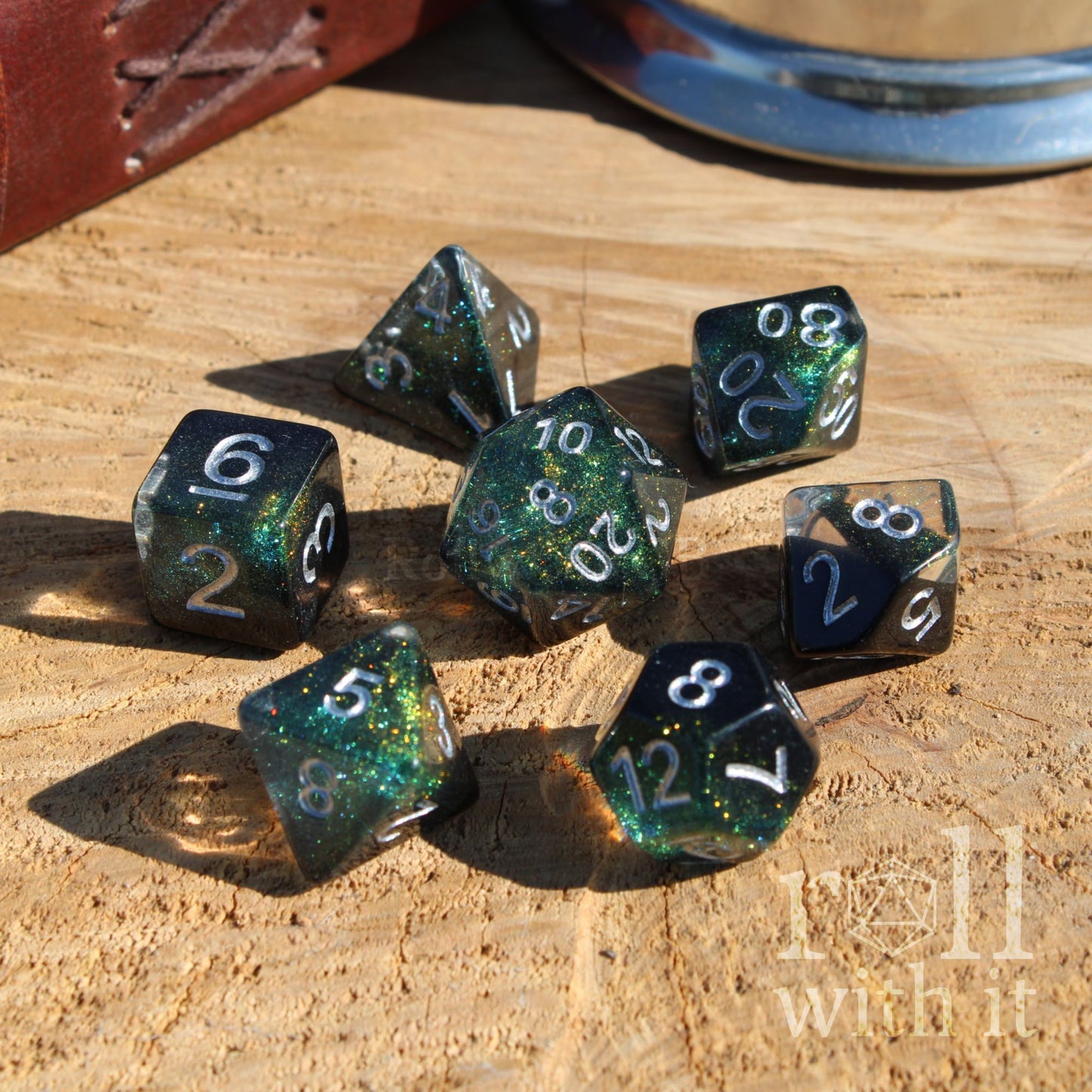 Set of black green blue silver star polyhedral dice on a wooden surface with 'roll with it' text.