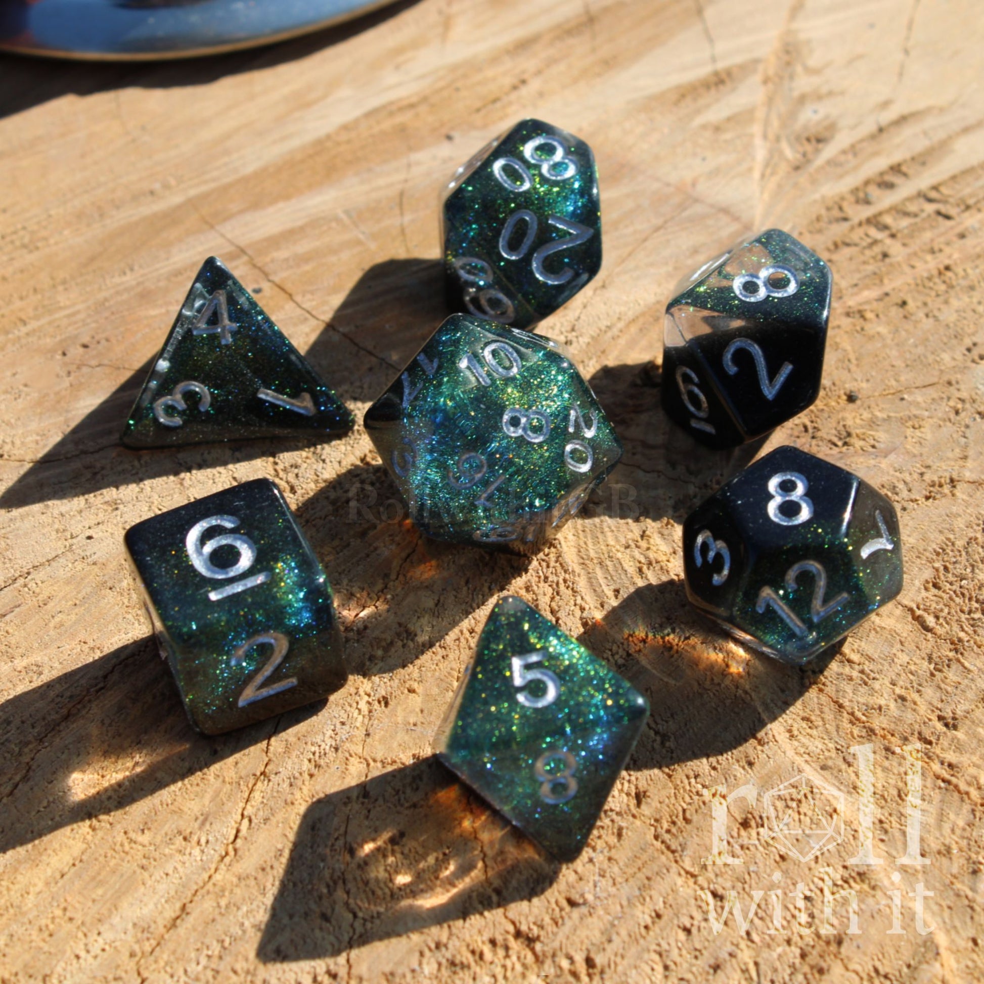 Set of glittery space black and glitter polyhedral dice on a wooden surface with 'roll with it' branding.