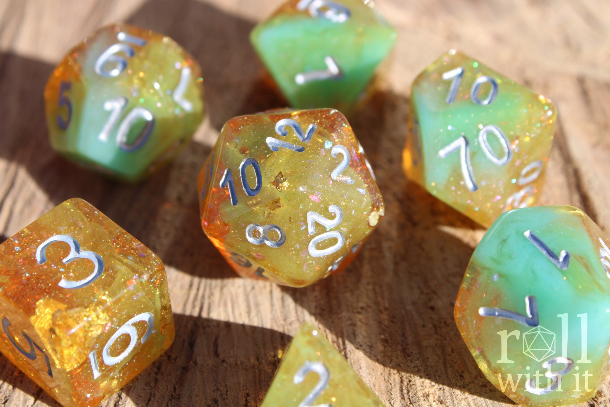 Set of colourful and glittery golden and teal polyhedral roleplaying DND dice with silver numbers on a wooden surface