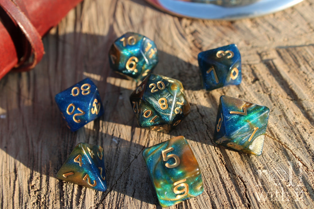 Set of glittery mixed blue, green, and gold polyhedral roleplaying dice on a wooden surface