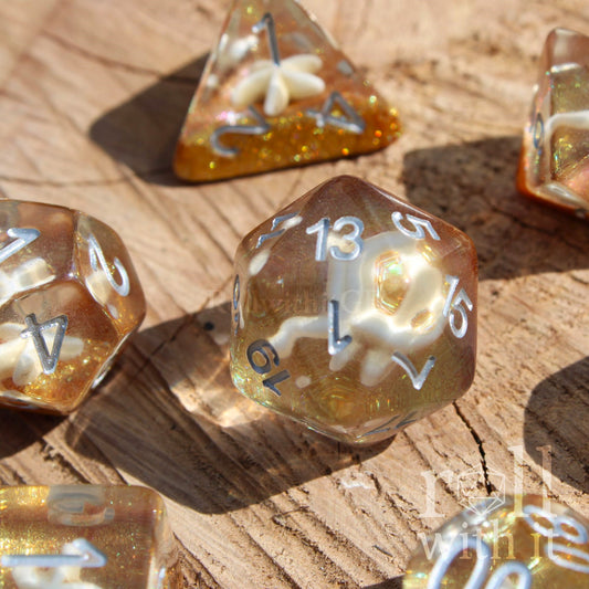Set of golden glittery sandy clear polyhedral dice with a seashell inside on a wooden surface