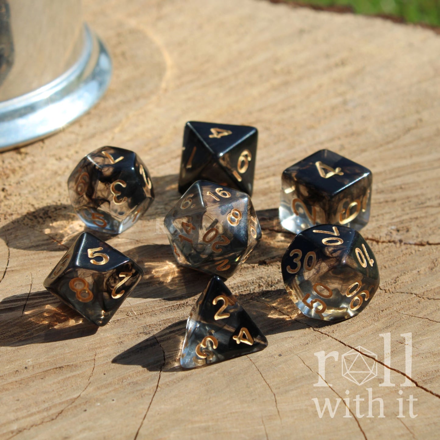 Set of metallic polyhedral dice on a wooden surface with 'roll with it' branding.
