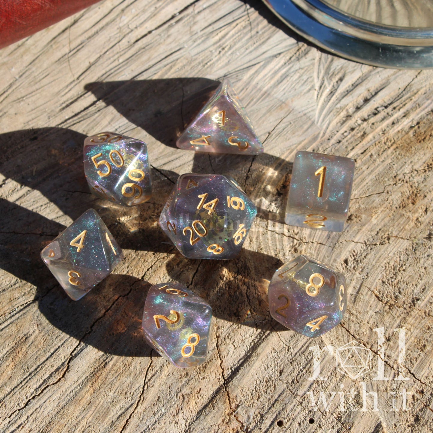 Top view of 7 polyhedral dnd dice on a wooden surface with a shiny glitter filled appearance and with golden numbers and gold cogs