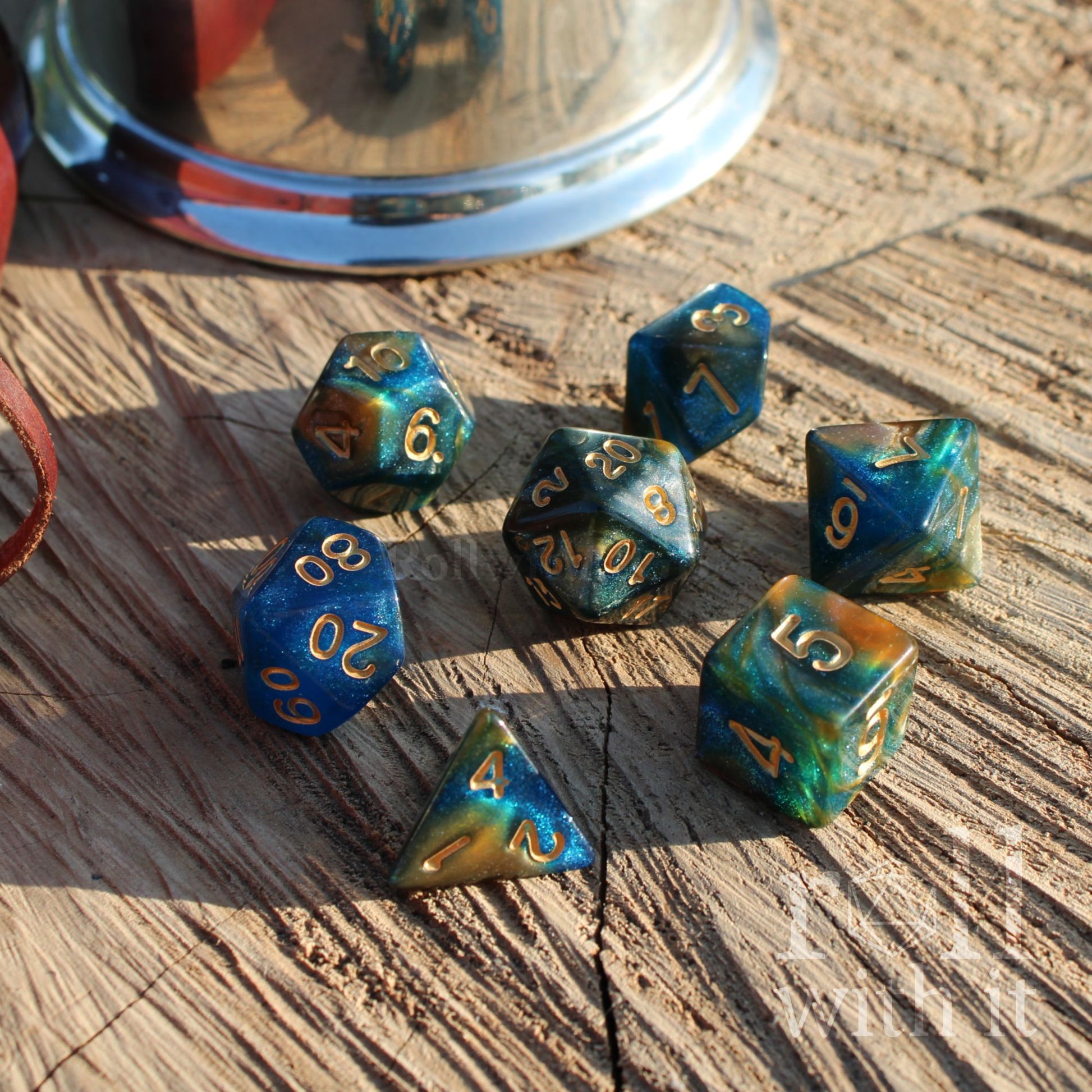 Set of blue and green polyhedral dice with gold numbers on a wooden surface.