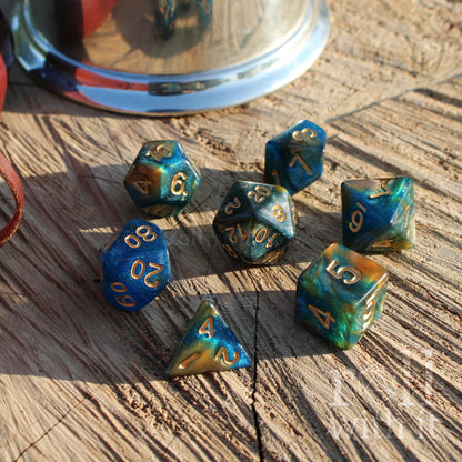 Set of blue and green polyhedral dice with gold numbers on a wooden surface.