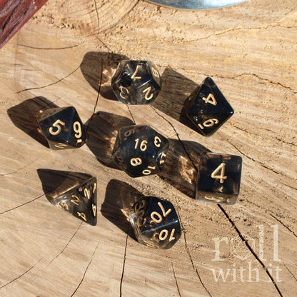 Set of black dice with gold numbers on a wooden surface, featuring the brand 'roll with it'.