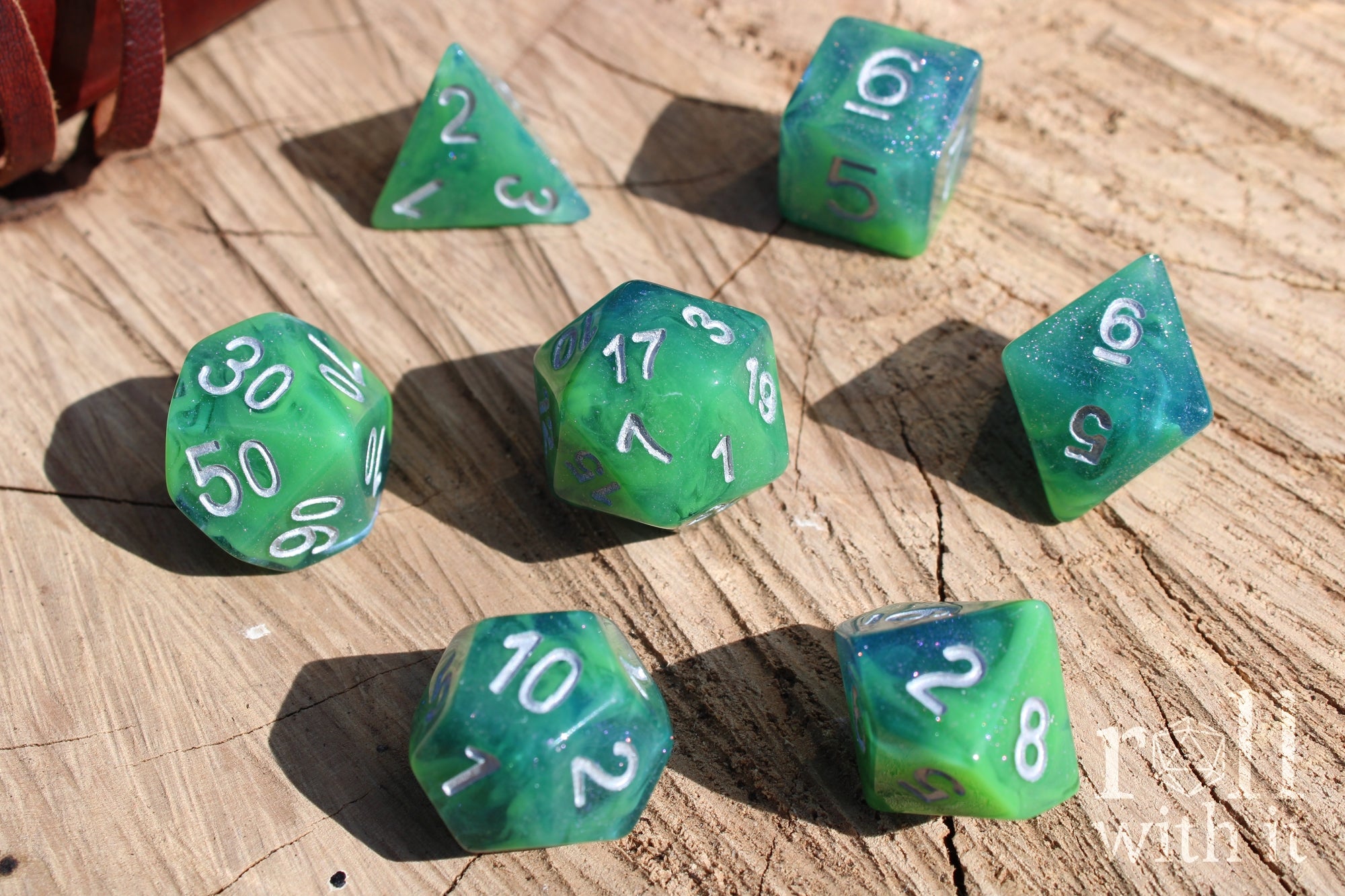 Set of green and blue glittery polyhedral DND dice with silver numbers on a wooden surface