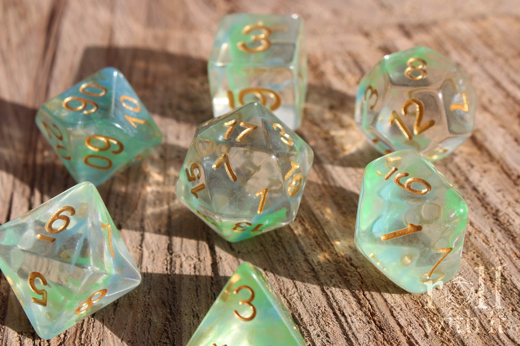 Set of green and pale blue clear polyhedral roleplaying dice with gold numbers on a wooden surface