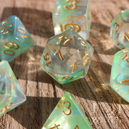 Set of green and pale blue swirling clear polyhedral roleplaying dice with gold numbers on a wooden surface