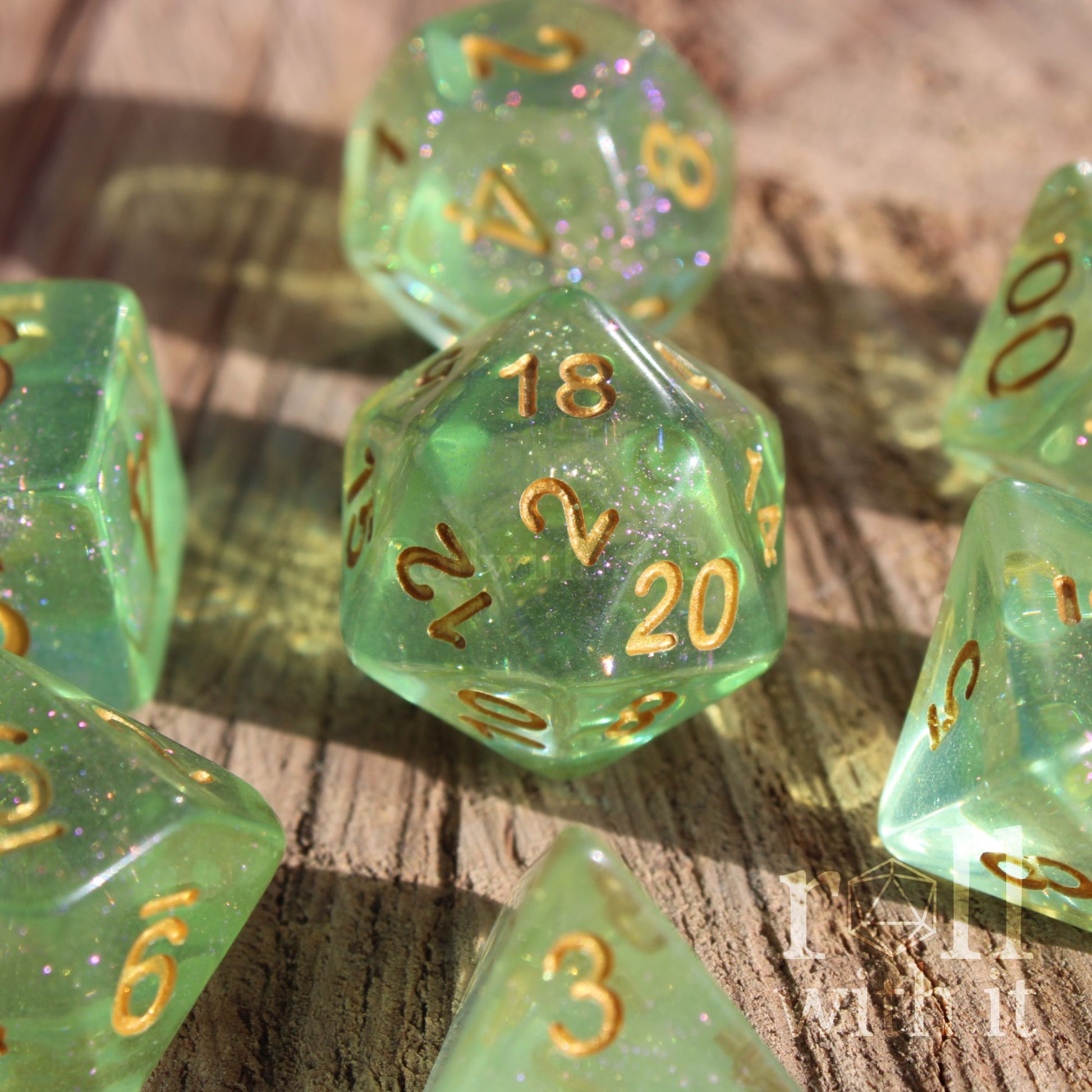 Set of green shimmering polyhedral roleplaying dice with gold numbers on a wooden surface