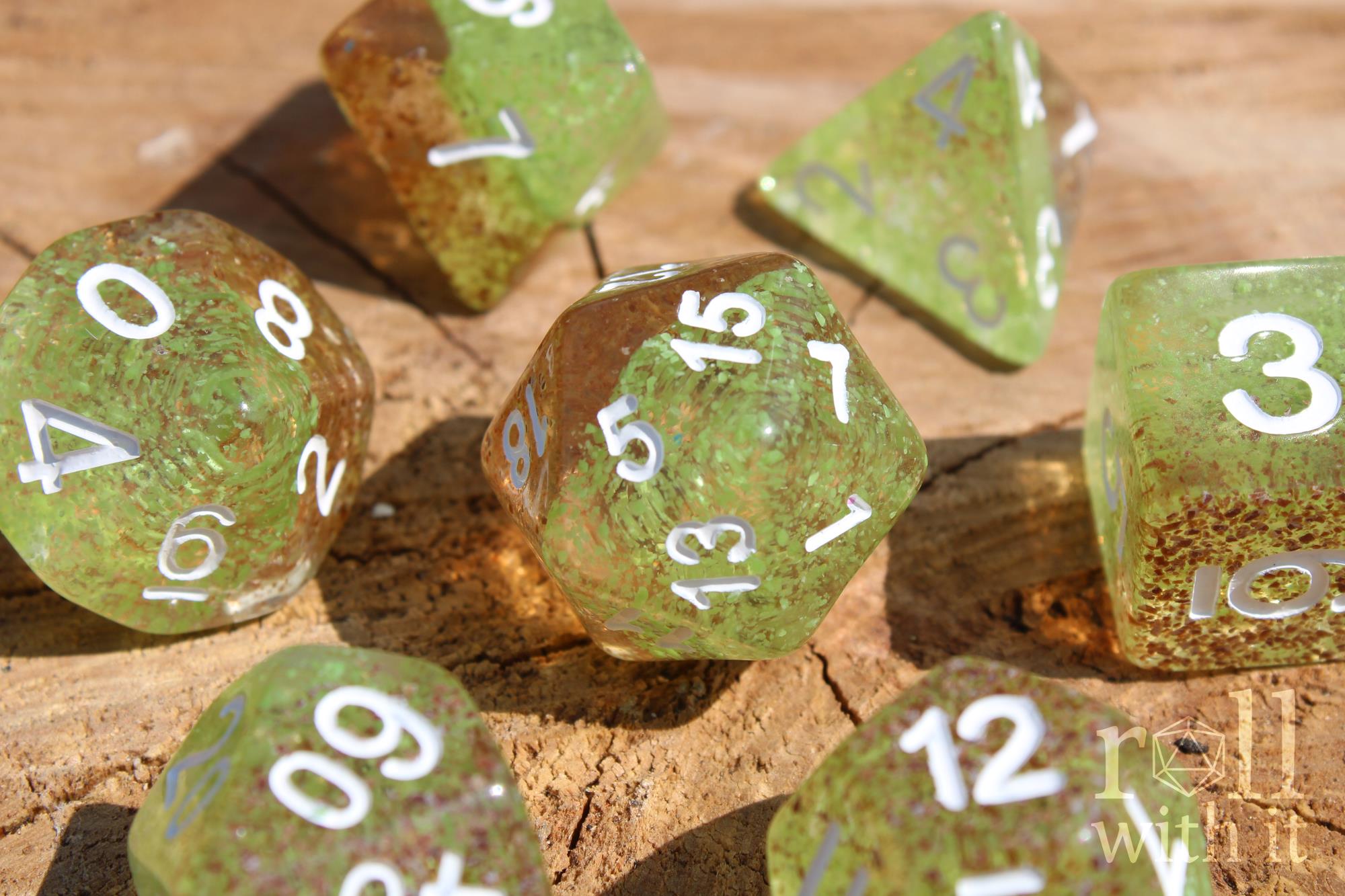 Apple green and ginger brown speckled polyhedral DND dice with white numbers sat on a wooden surface