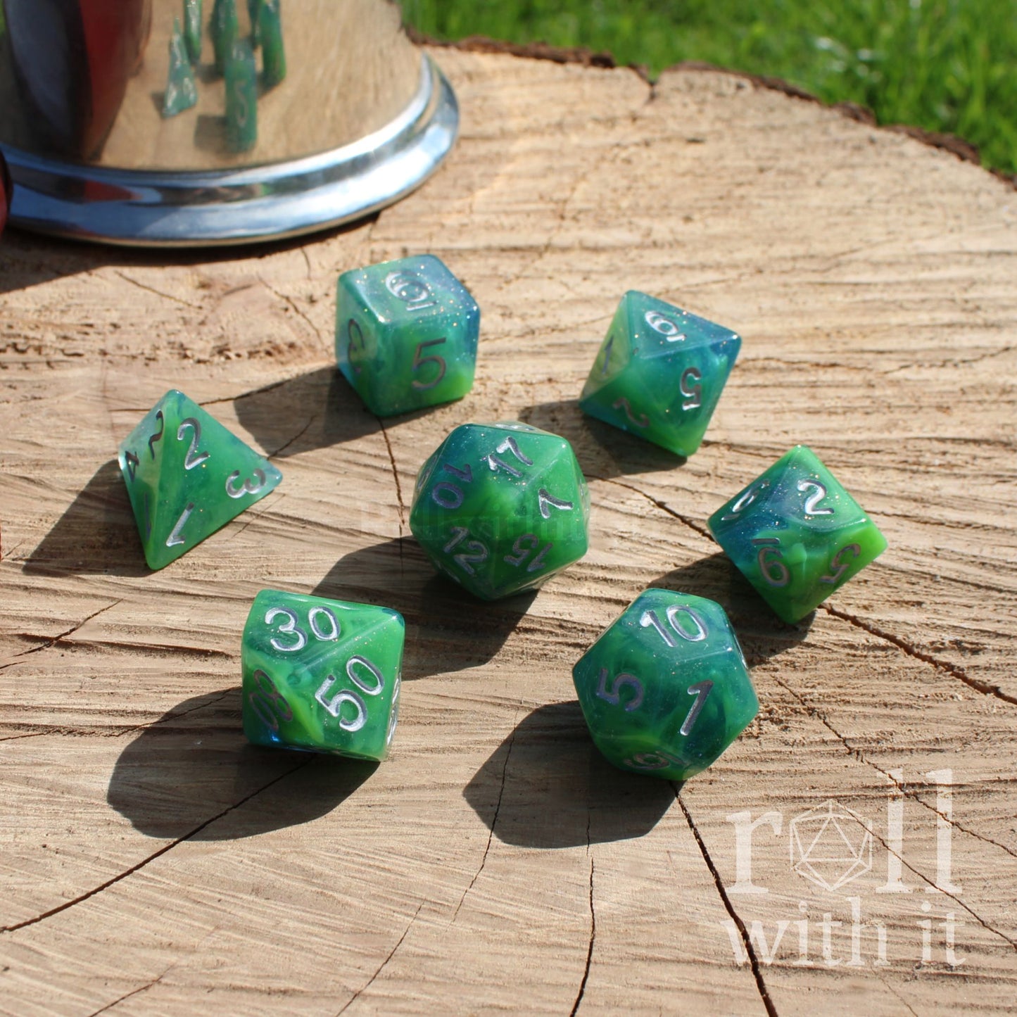 Green teal silver letters polyhedral dice set on a wooden surface with 'roll with it' branding.
