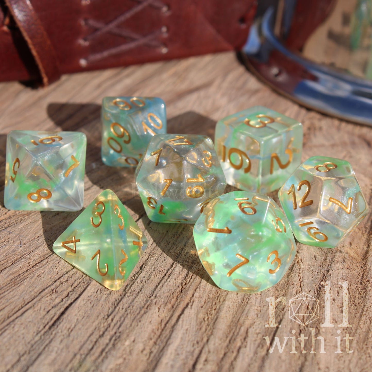 Set of green fantasy tabletop roleplaying polyhedral dice with gold numbers on a wooden surface, featuring the text 'roll with it'.