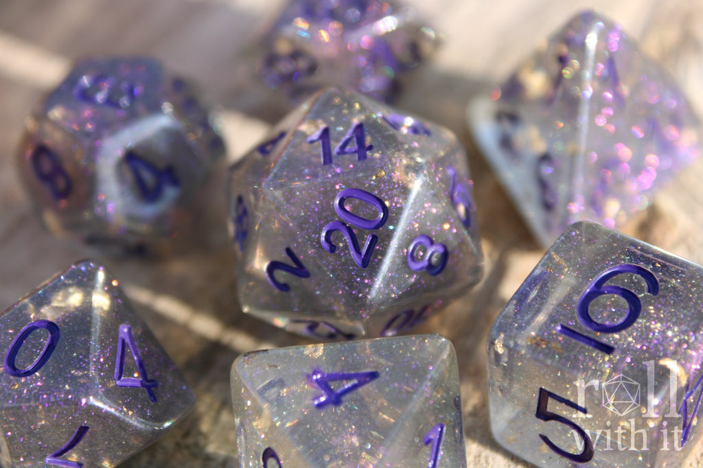 Set of grey shimmering and star like polyhedral dice with gold foil and purple numbers on a wooden background