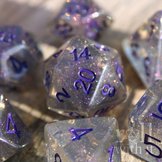 Set of grey shimmering and star like polyhedral dice with gold foil and purple numbers on a wooden background