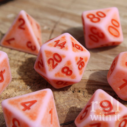 Set of matte pink polyhedral dice with red numbers on a wooden surface