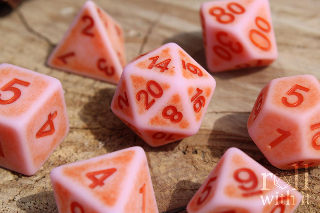 Set of matte pink polyhedral dice with red numbers on a wooden surface