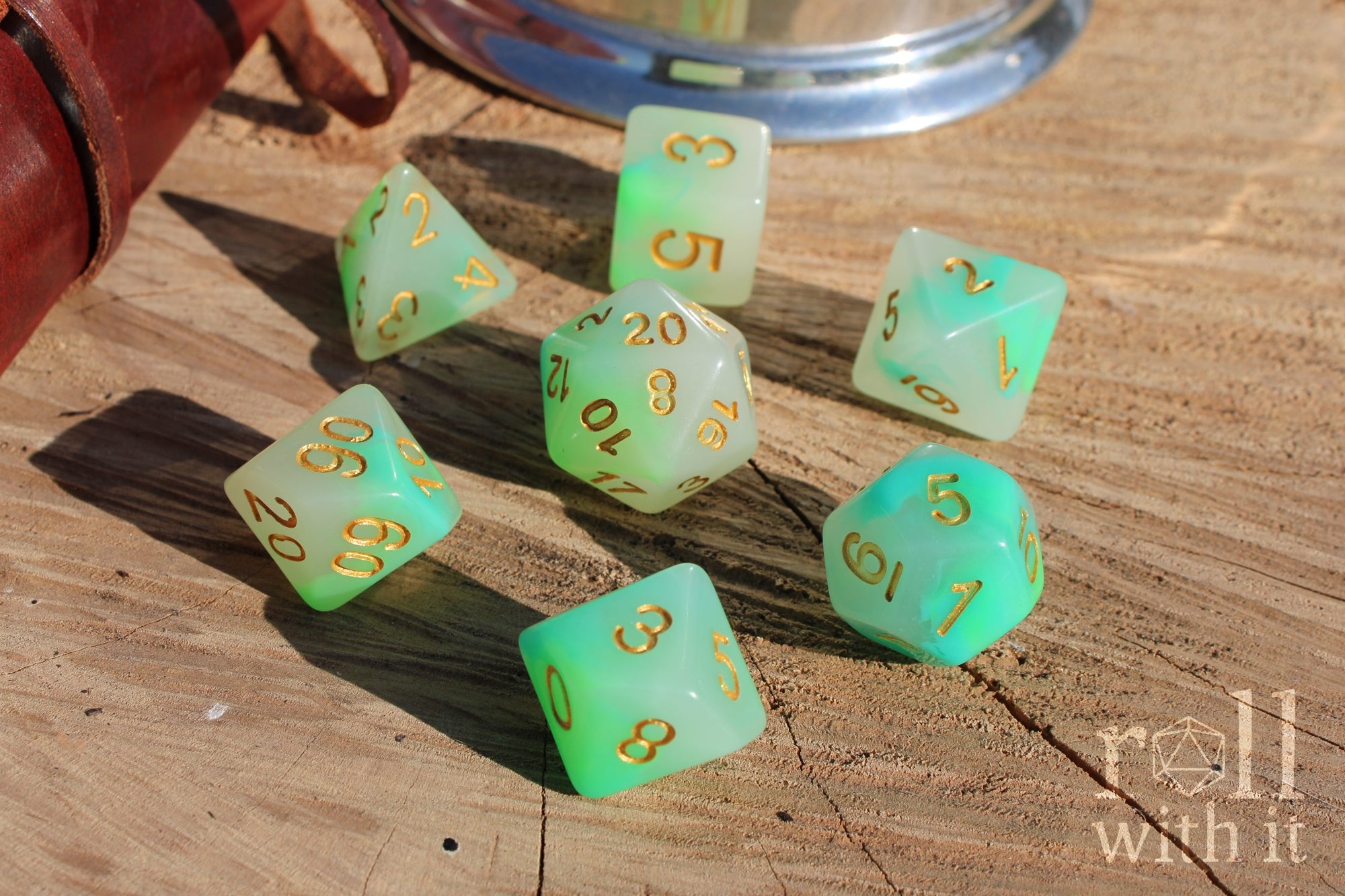 Set of turquoise and green polyhedral DND dice with gold numbers on a wooden surface