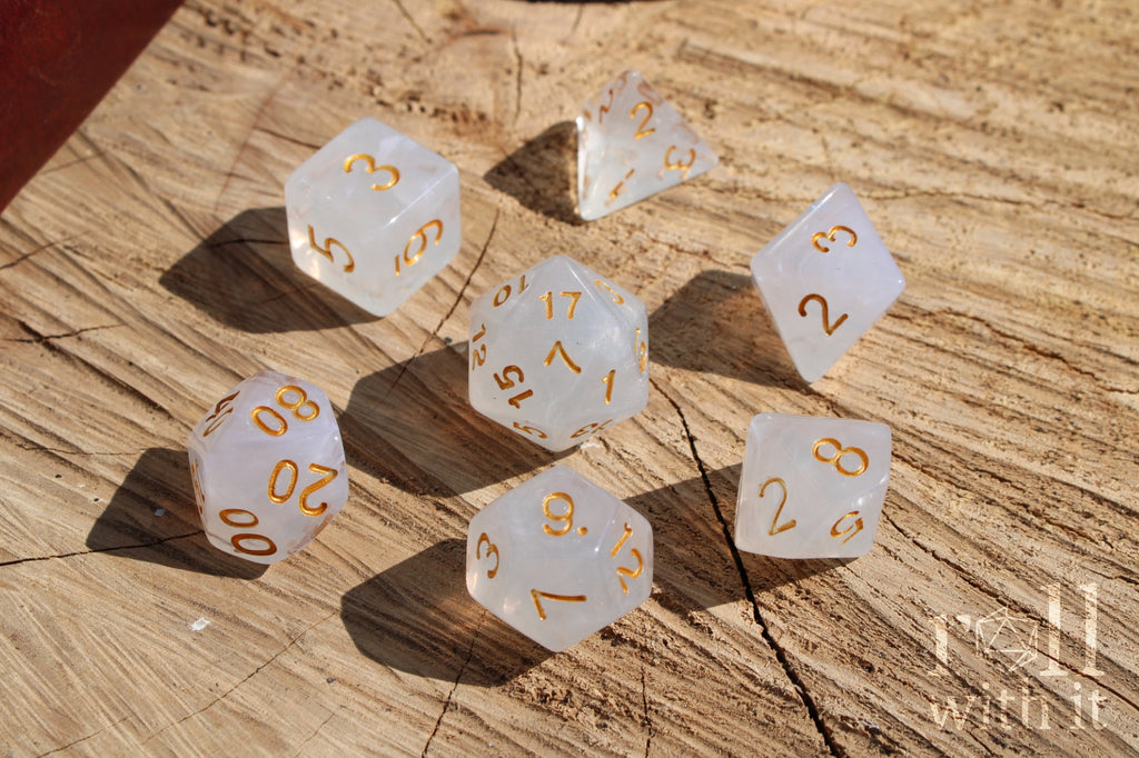 A set of silver grey polyhedral roleplaying dice with gold numbers on a wooden surface