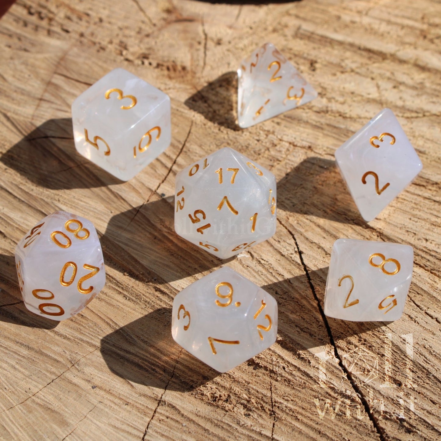 A set of 7 silver grey polyhedral D&D roleplaying dice with gold numbers on a wooden surface