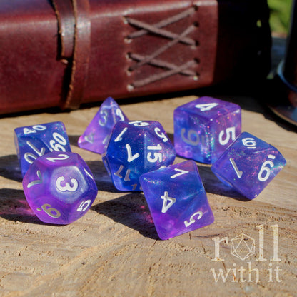Side view of 7 purple and blue TTRPG pathfinder dice set on a wooden surface with 'roll with it' branding.
