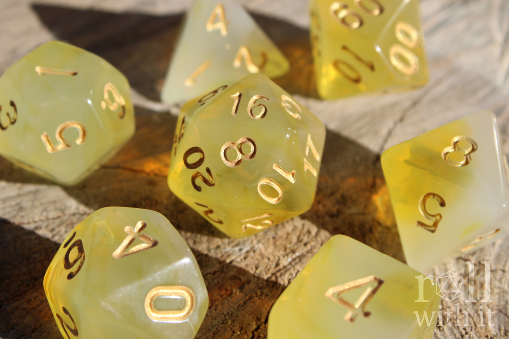Set of translucent lemon yellow polyhedral roleplaying dice with gold numbers on a wooden surface.