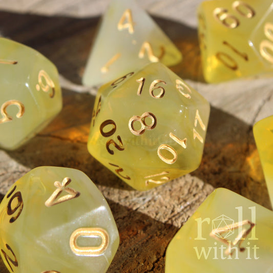 Set of 7 cute translucent lemon yellow polyhedral roleplaying tabletop dice with gold numbers on a wooden surface.