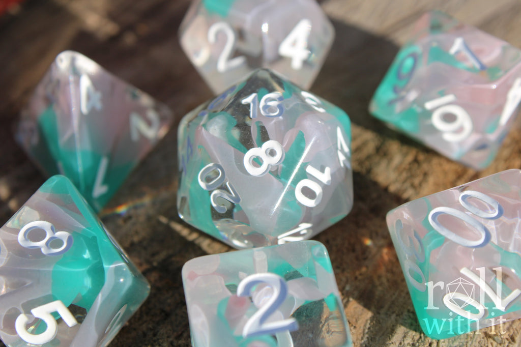 Set of light blue turquoise and white polyhedral roleplaying dice with white numbering on a wooden surface