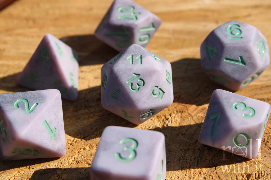Lilac purple matte polyhedral role-playing dice with mint green numbers on a wooden surface
