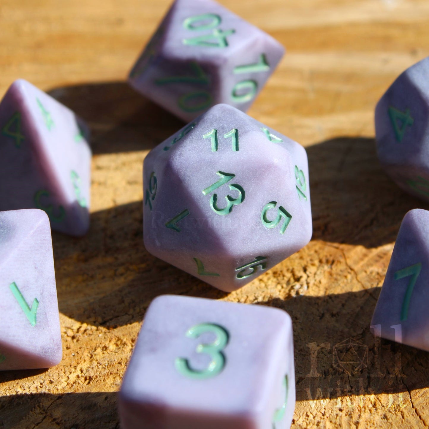 Lilac purple matte polyhedral role-playing dice with mint green numbers on a wooden surface