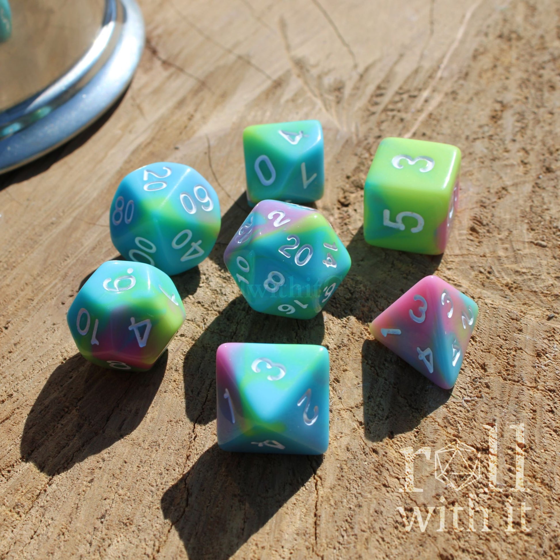Angled view of 7 pastel rainbow fantasy aesthetic DND polyhedral resin dice on a wooden surface with white numbers