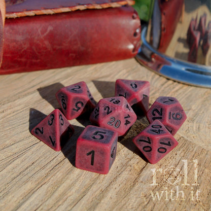 Set of red matte polyhedral dice on a wooden surface with 'roll with it' text.