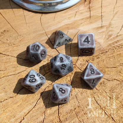 Top view of 7 matte silver D&D dice with dark black details and numbering on a wooden surface