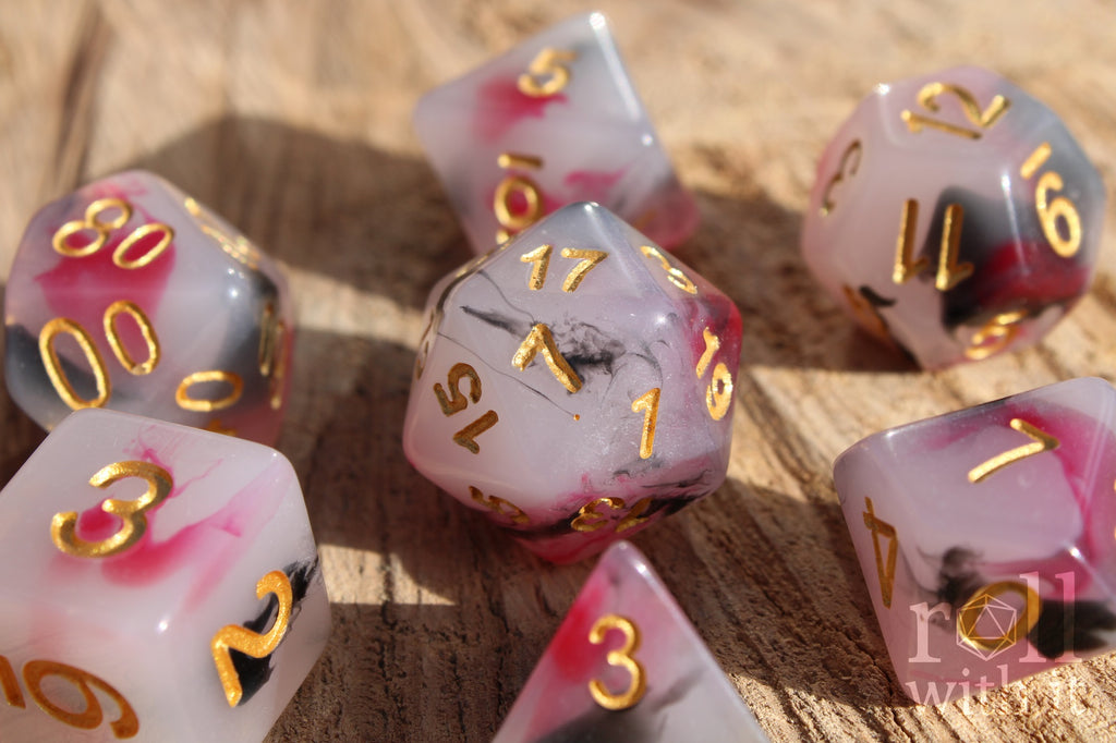 Set of black, red, and creamy white roleplaying dice with marbled design and gold numbers on a wooden surface