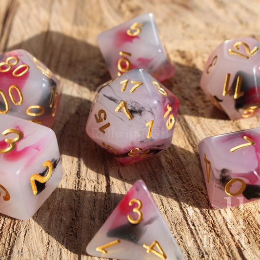 Set of pink white black clowncore dice with gold numbers on a wooden surface