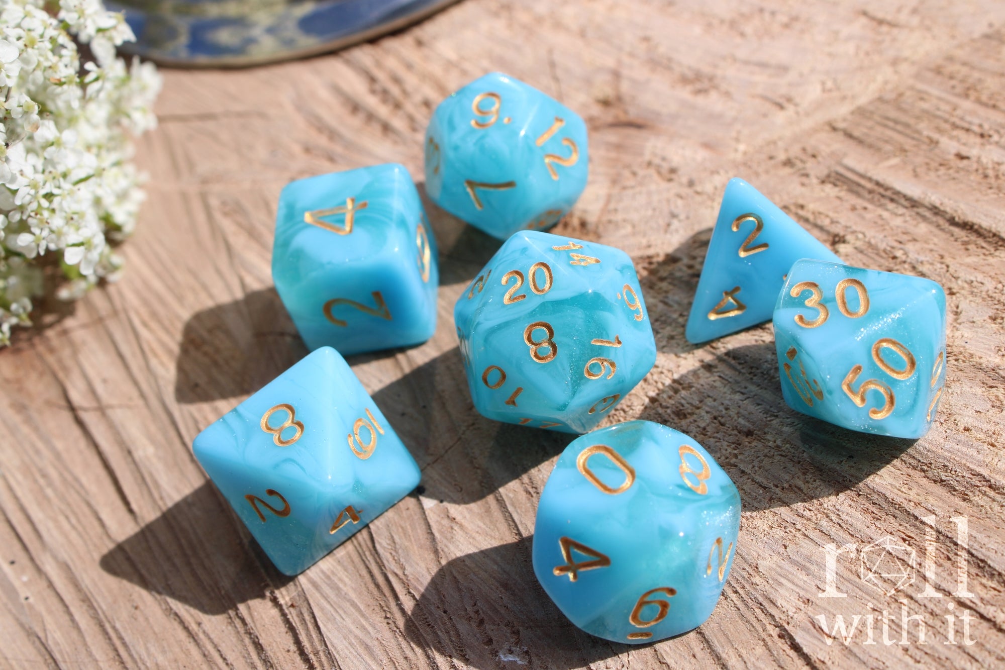 Set of aqua blue polyhedral roleplaying dice with gold numbers on a wooden surface.