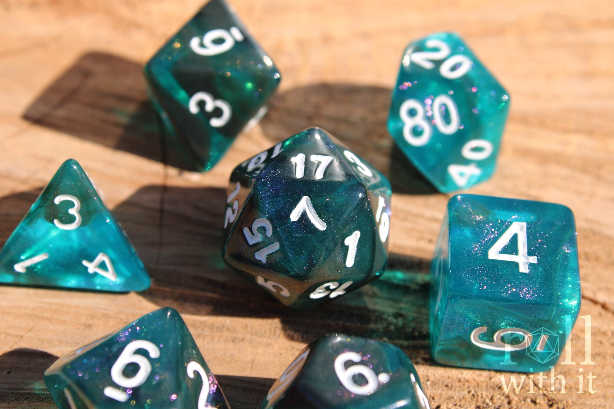 Teal and black glittery polyhedral roleplaying dice set with white numbers on a wooden surface
