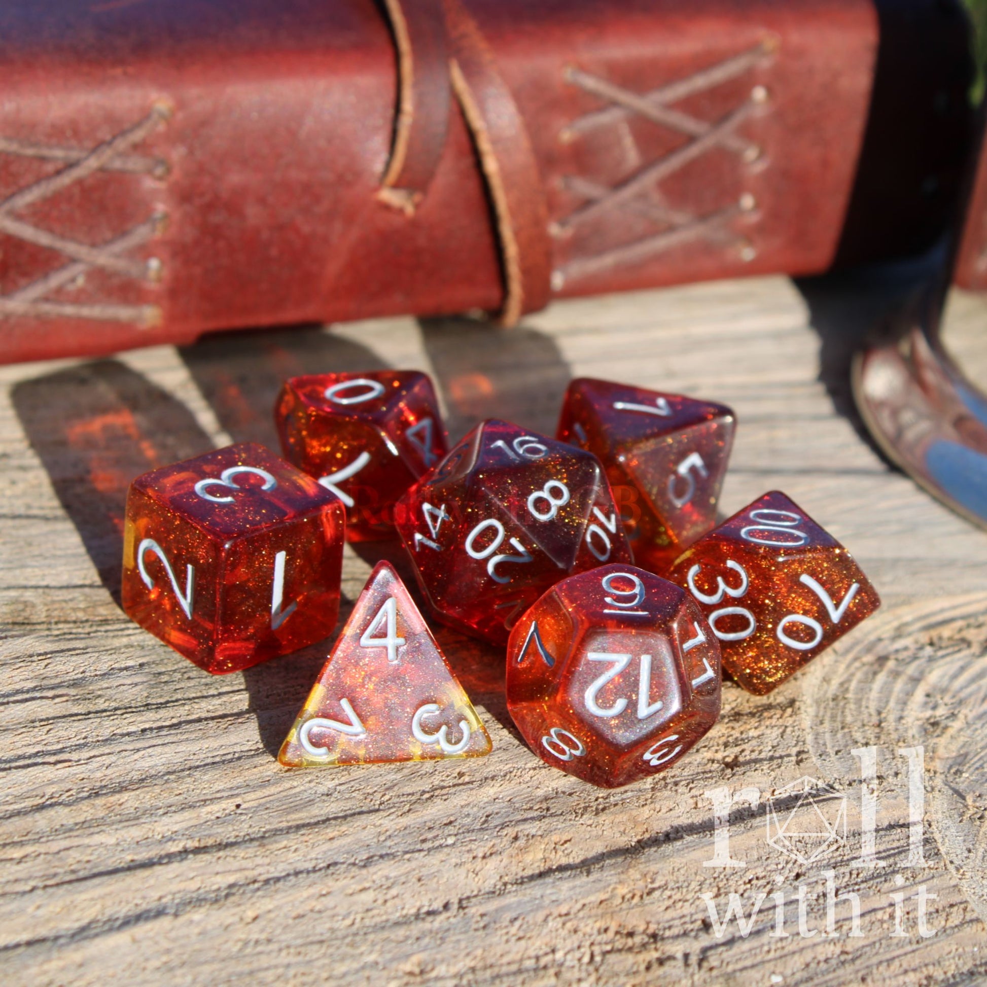 Set of red and orange bright polyhedral dice on a wooden surface with a leather-bound book in the background.