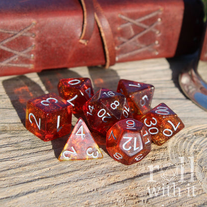Set of red and orange bright polyhedral dice on a wooden surface with a leather-bound book in the background.