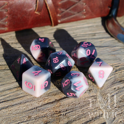Set of 7 pink black pale goth polyhedral D&D dice with pink numbers on a wooden surface